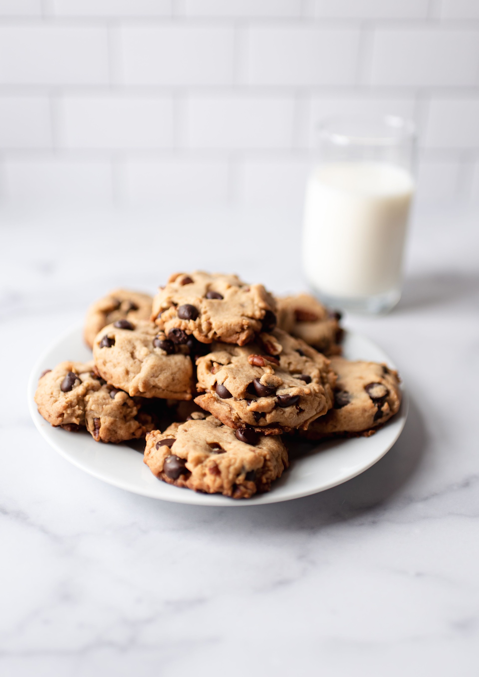 Plate of chocolate chip cookies and milk on white marble counter.